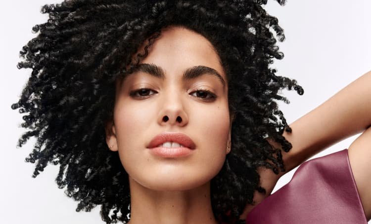 Woman posing and showcasing her well-defined dark coily hair with a healthy look, bounce, and natural texture enhancement