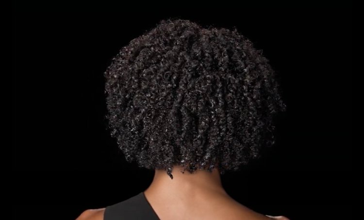 Woman from behind with shiny, healthy coily hair, illustrating tips and techniques to detangle curls without causing damage.
